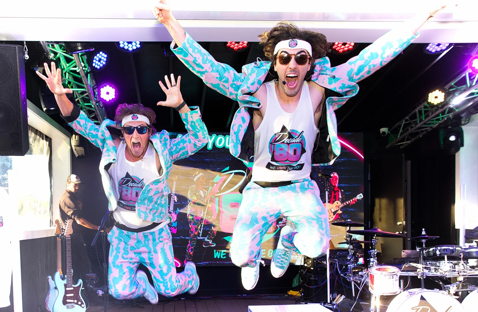Two Decade80 bandmates jumping on stage in pastel suits