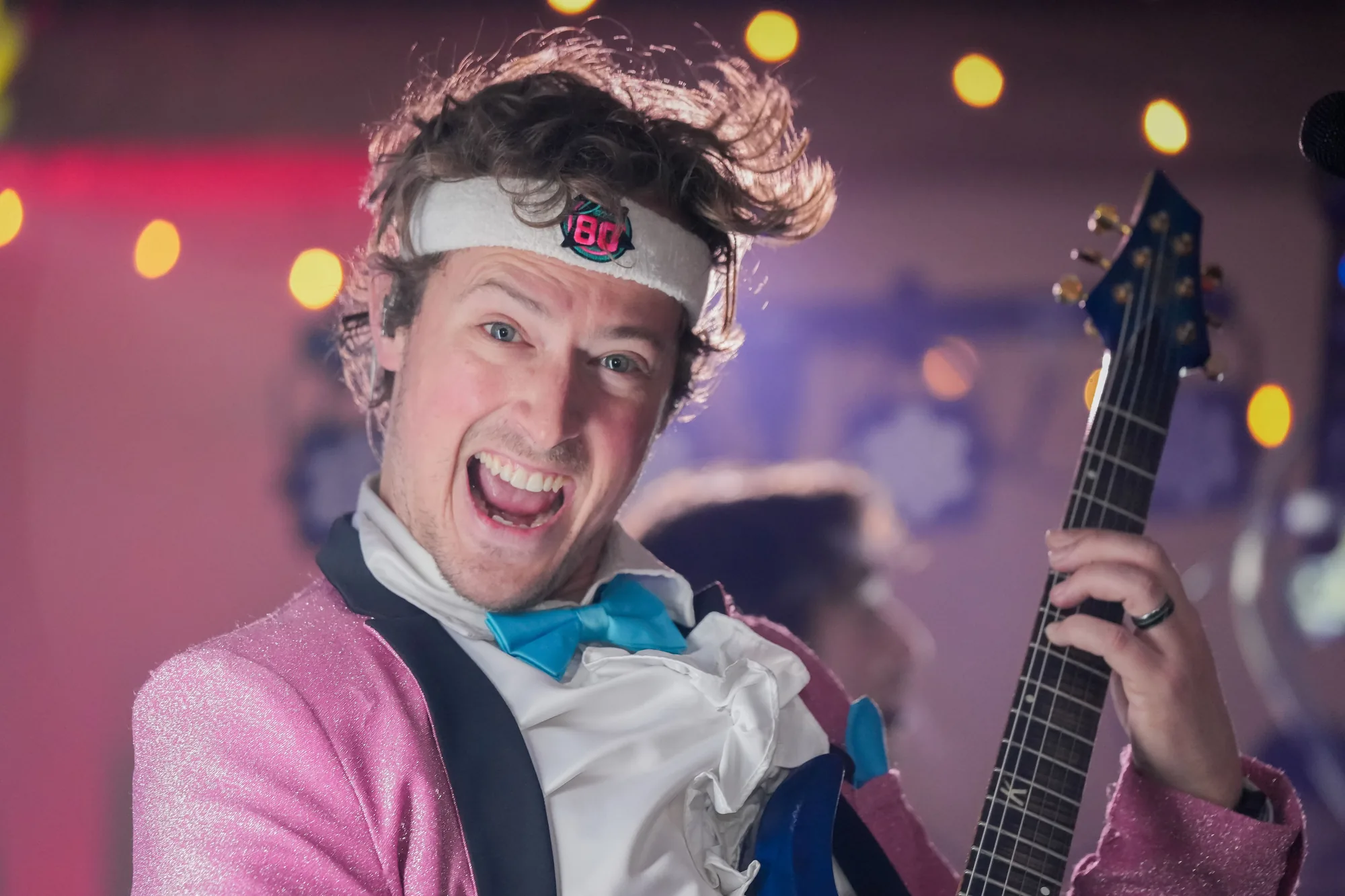 Decade80 guitarist grinning in his headband and pink tuxedo